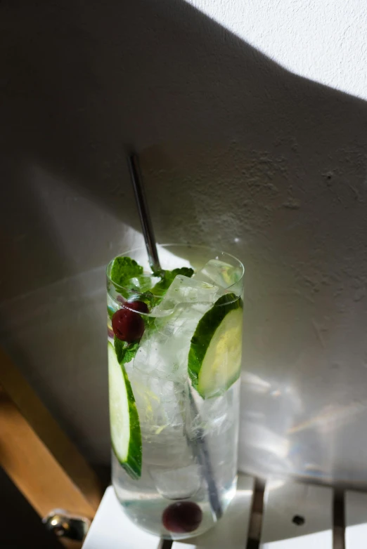 a glass filled with a drink sitting on top of a table, cucumber, long street, silver light, angled