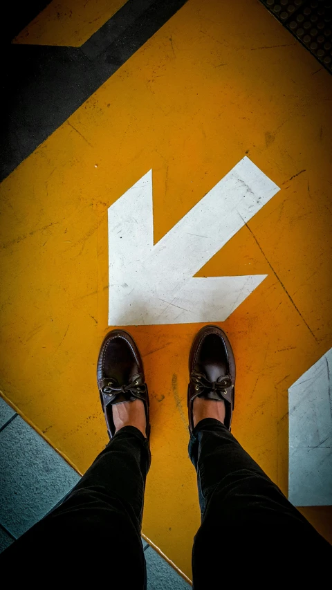 a person standing on top of a yellow floor next to a white arrow, by Matt Stewart, trending on pexels, shoe, brown, thumbnail, signs