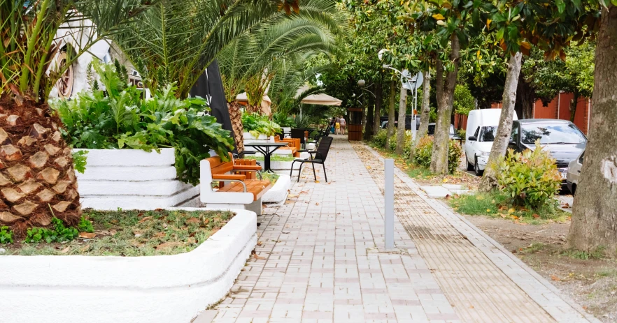 a sidewalk lined with tables and chairs next to palm trees, by Zofia Stryjenska, unsplash, with lots of vegetation, greece, public art, 15081959 21121991 01012000 4k