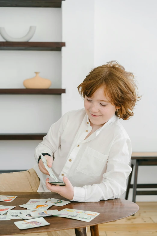 a woman sitting at a table playing a card game, an album cover, trending on pexels, red haired teen boy, scanning items with smartphone, wearing white shirt, little kid