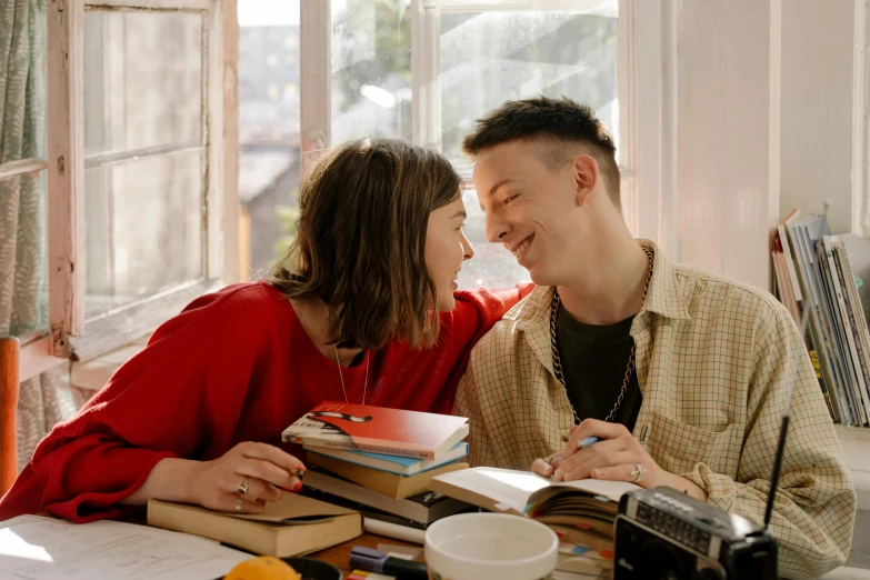 a man and a woman sitting at a table with books, a photo, by Julia Pishtar, pexels, happening, lesbian embrace, smiling slightly, looking outside, julian ope