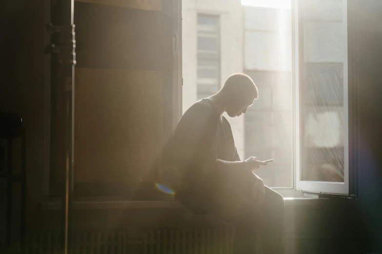 a man sitting on a window sill looking at his cell phone, trending on unsplash, happening, dappled sunlight, ignant, people at work, dusty light