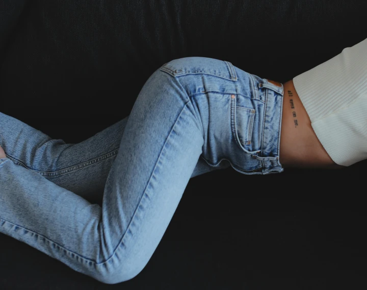 a woman laying on top of a black couch, a tattoo, inspired by Elsa Bleda, trending on pexels, jeans pants, detailed product image, skintight, bella poarch