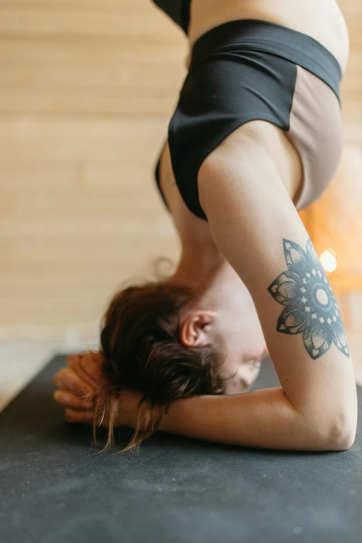 a woman doing a handstand on a yoga mat, a tattoo, pexels contest winner, resting head on hands, pixeled stretching, arched back, photograph of a sleeve tattoo