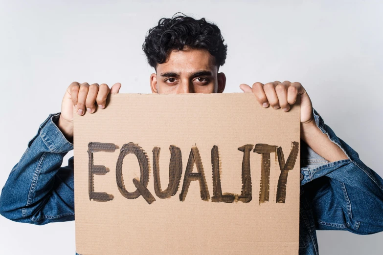 a man holding a cardboard sign that says equality, trending on pexels, renaissance, background image, indian, billy butcher, “hyper realistic