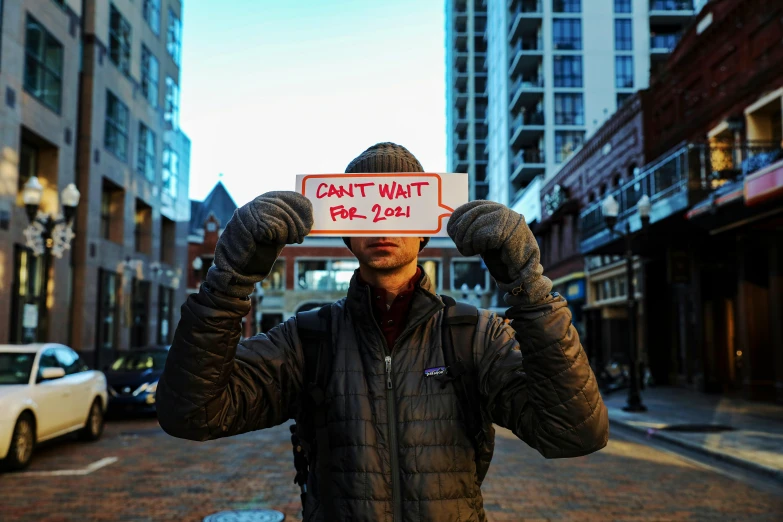 a man holding a sign in front of his face, an album cover, by Matt Cavotta, pexels contest winner, gen z, do what we can, january 20th, from wheaton illinois