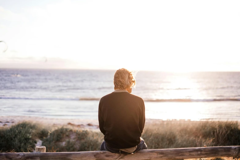 a person sitting on top of a wooden bench, unsplash, looking out at the ocean, older male, soft warm light, al fresco