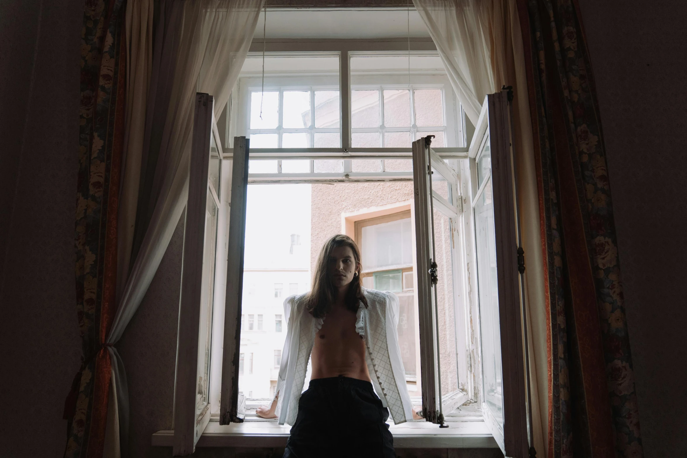 a woman that is standing in front of a window, inspired by Elsa Bleda, unsplash, aestheticism, white russian clothes, open shirt, androgynous male, hotel room