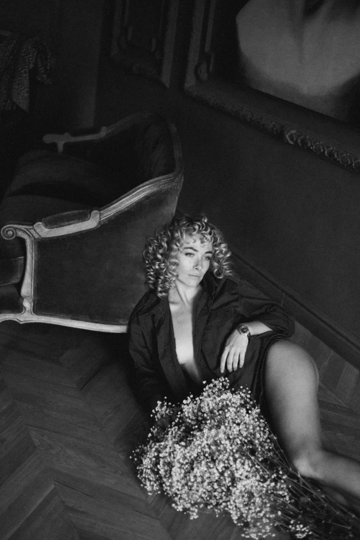 a black and white photo of a woman laying on the floor, an album cover, pexels contest winner, photorealism, curly blonde hair, flowers, sitting in an armchair, cinematic outfit photo