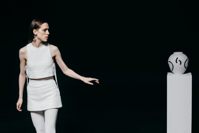 a woman standing in front of a sculpture, inspired by Vanessa Beecroft, unsplash, minimalism, 3 actors on stage, emma watson, white outfit, on black background