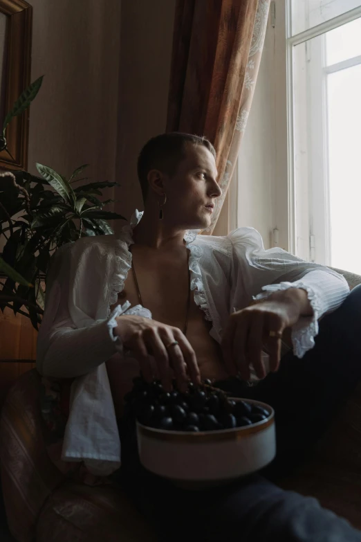 a man sitting in a chair holding a bowl of berries, an album cover, unsplash, renaissance, beautiful androgynous girl, anna podedworna, low quality footage, ignant