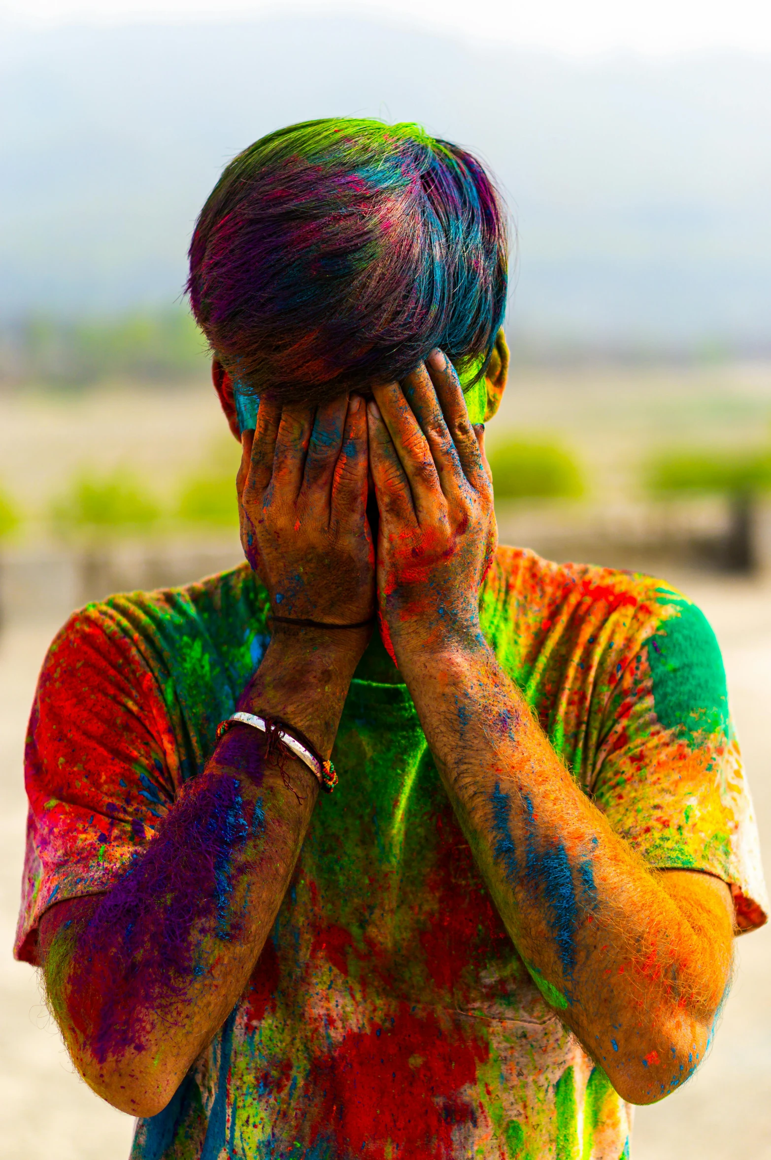 a man covering his face with his hands, a colorized photo, trending on pexels, color field, tribal paint, lgbt, covered in dust, festive colors