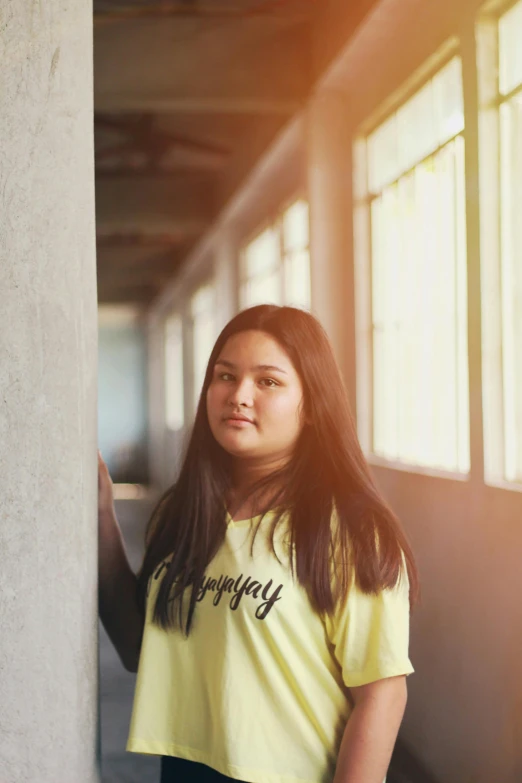 a woman in a yellow shirt leaning against a wall, inspired by Kim Jeong-hui, unsplash, portrait of teenage girl, backlight photo sample, in school hallway, shot on sony a 7