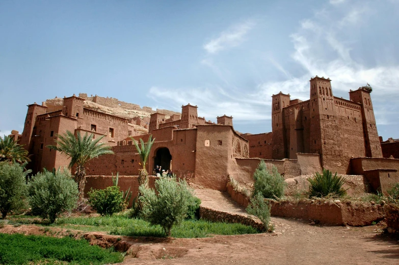 a large brown building sitting on top of a lush green field, inspired by Alberto Morrocco, pexels contest winner, les nabis, moroccan, the red citadel, in a dusty red desert, high walls