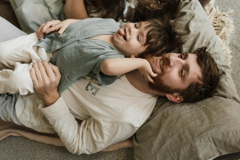 a man laying on top of a bed next to a child and a dog, pexels contest winner, incoherents, bearded, brunette boy and redhead boy, father holds child in the hand, australian