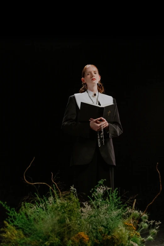 a woman standing on top of a lush green field, an album cover, inspired by Vanessa Beecroft, unsplash, renaissance, in a black suit, dressed like a cleric, on stage, still frame from a movie