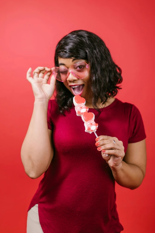 a woman holding a lollipop in front of her face, pexels, on a red background, woman with rose tinted glasses, made of candy and lollypops, red hearts