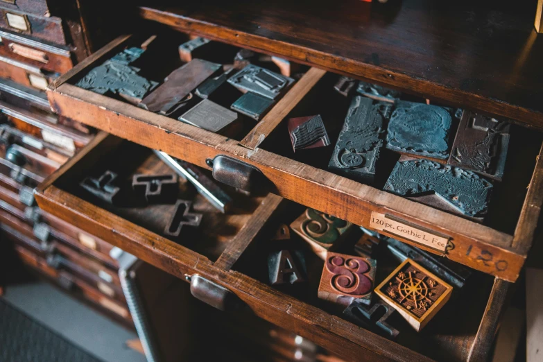 a drawer that has some type of stamps in it, a woodcut, unsplash, old furnitures, items and gadget, metal works, contain