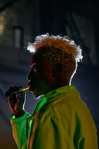a man in a green jacket smoking a cigarette, an album cover, inspired by Godfrey Blow, pexels, afrofuturism, yellow spiky hair, live performance, glowing with colored light, (night)