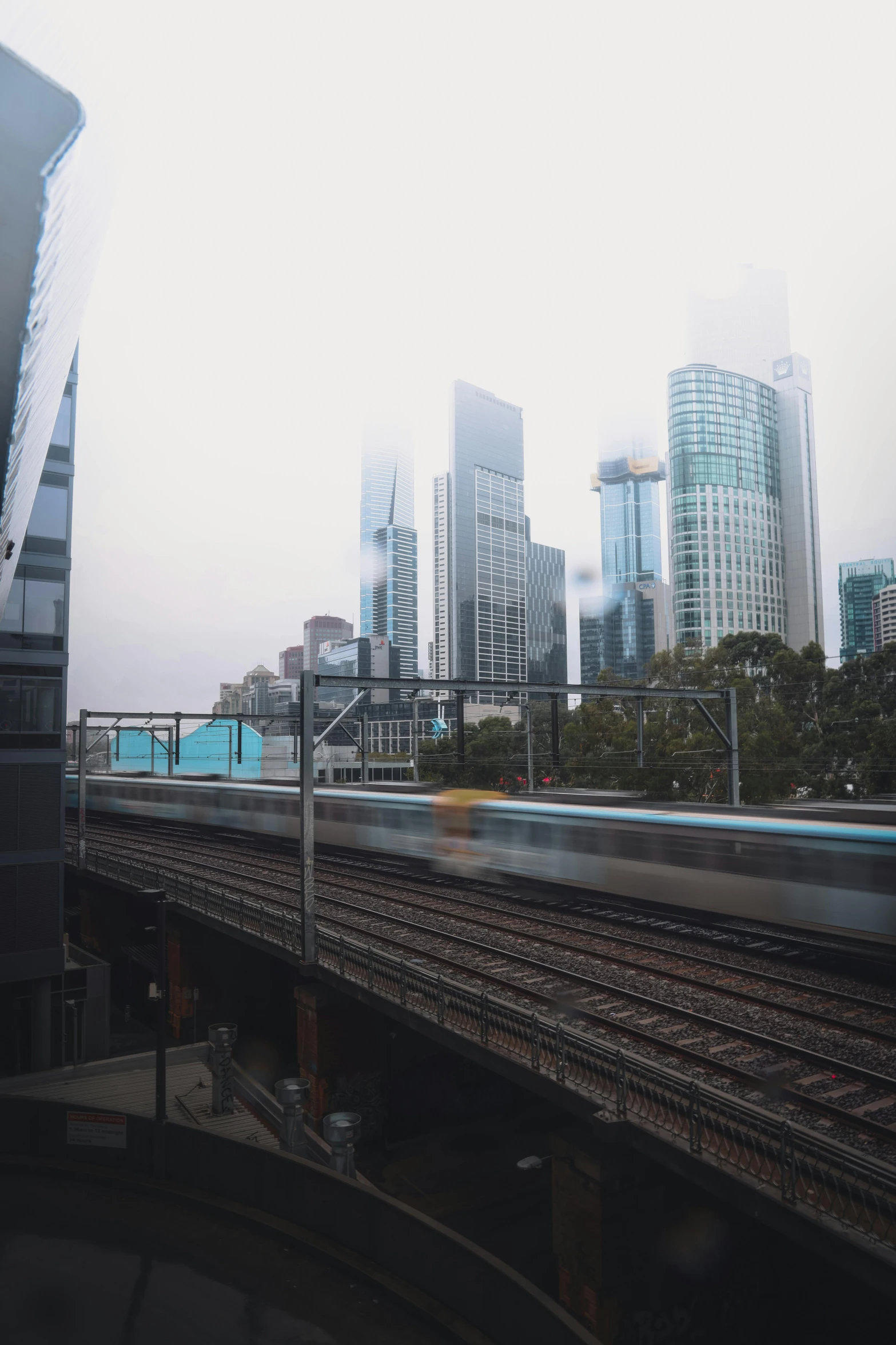 a train traveling through a city next to tall buildings, a picture, inspired by Sydney Carline, unsplash contest winner, overcast, low quality photo, cinematic view!!!, slightly foggy