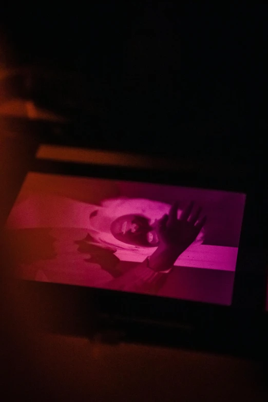 a laptop computer sitting on top of a table, a hologram, inspired by Elsa Bleda, video art, barely lit warm violet red light, abstract people in frame, darkroom, xerography