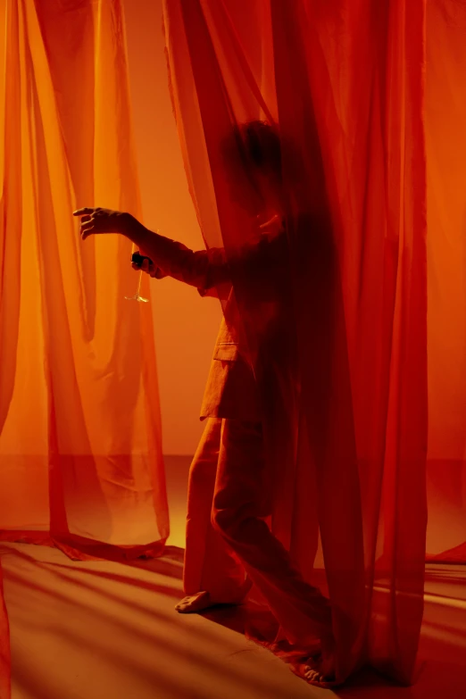 a man standing in front of a red curtain, inspired by Georges de La Tour, pexels contest winner, conceptual art, orange yellow ethereal, showstudio, dress in voile, musician