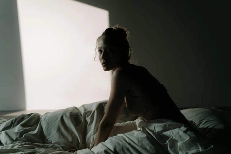 a woman sitting on top of a bed in a dark room, inspired by Elsa Bleda, unsplash contest winner, australian tonalism, with the sun shining on it, her face is in shadow, sydney sweeney, sunfaded