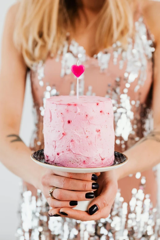 a woman holding a pink cake with a heart on top, metallic flecks, zoomed in, tall, feature