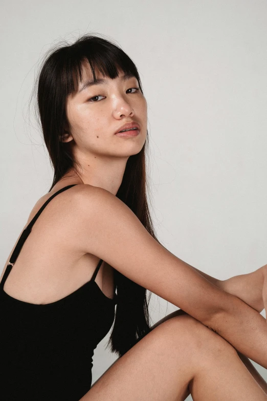 a woman sitting on the floor with her legs crossed, inspired by Kim Tschang Yeul, trending on pexels, wearing a cropped black tank top, gemma chan girl portrait, iris compiet, skincare