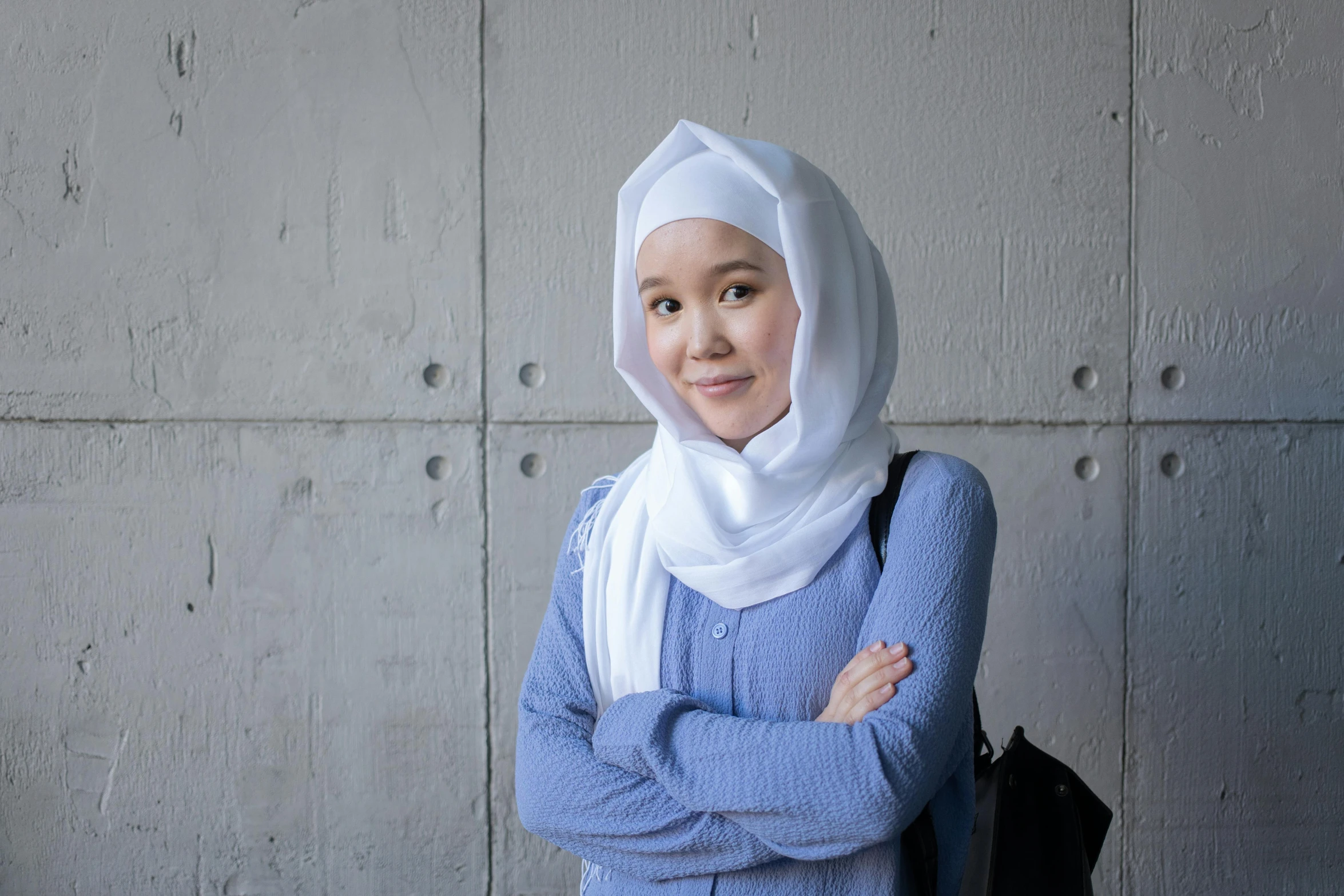 a woman standing in front of a concrete wall, inspired by Nazmi Ziya Güran, unsplash, hurufiyya, wearing a light blue shirt, white scarf, post graduate, she is korean
