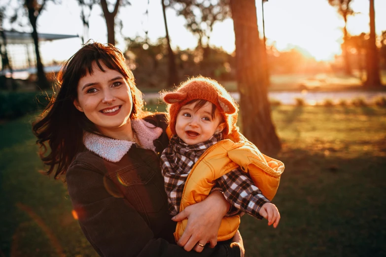 a woman holding a baby in her arms, by Julia Pishtar, pexels, golden hour 8k, both smiling for the camera, avatar image, sunny day in a park