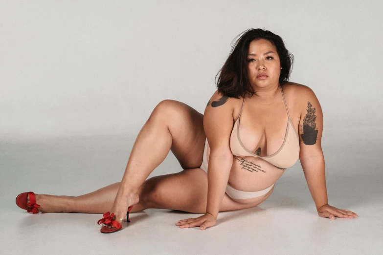 a woman with tattoos is sitting on the floor, pexels contest winner, curvy body, asian descent, set against a white background, wearing loincloth