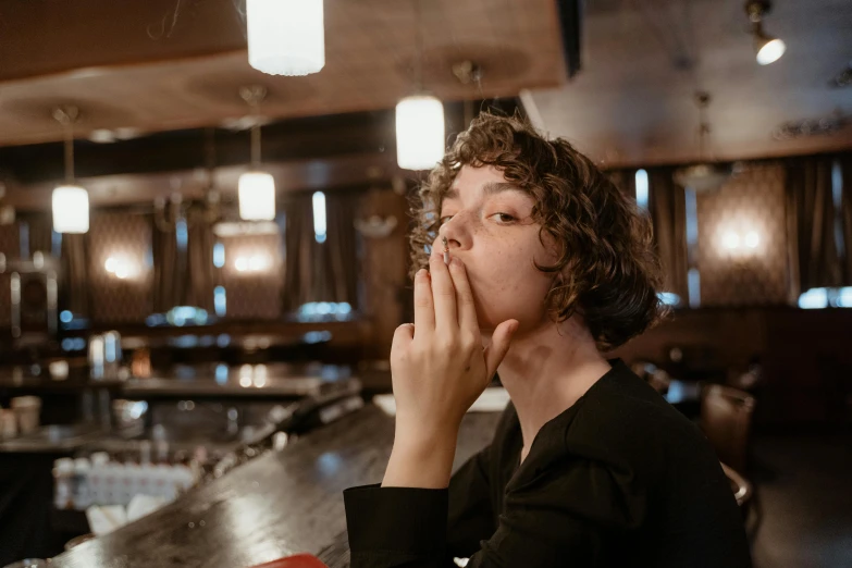 a woman sitting at a table in a restaurant, by Julia Pishtar, pexels contest winner, happening, finn wolfhard, thinker pose, sitting at the bar, hand over mouth