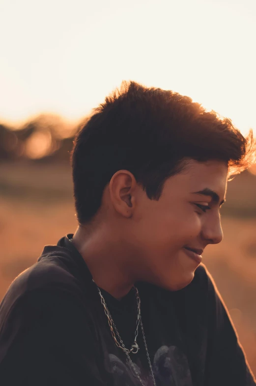 a young man sitting on top of a grass covered field, an album cover, trending on unsplash, backlit beautiful face, 14 yo berber boy, headshot profile picture, detailed face of a asian boy