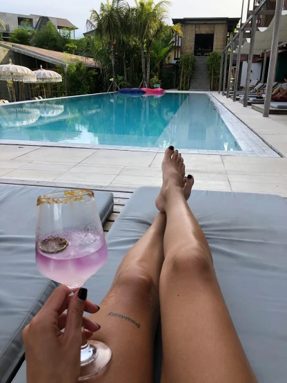 a woman sitting next to a swimming pool holding a wine glass, wearing pink flip flops, in sao paulo, lounge, profile image