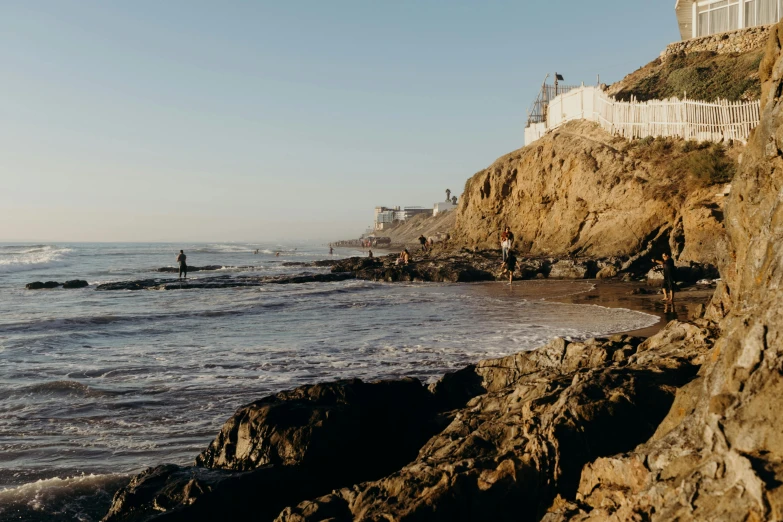 a group of people standing on top of a beach next to the ocean, by Carey Morris, unsplash contest winner, cliffside town, surfing, slightly sunny, background image