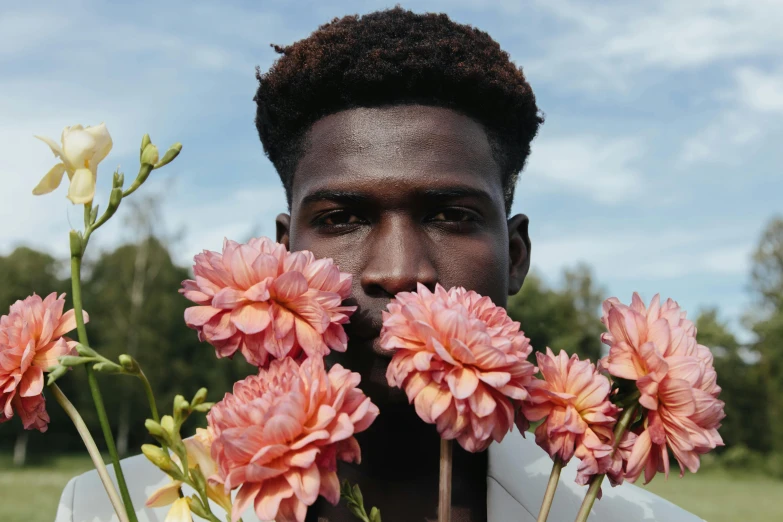 a man holding flowers in front of his face, by Carey Morris, pexels contest winner, brown skinned, looking to the right, portrait of tall, midsommar