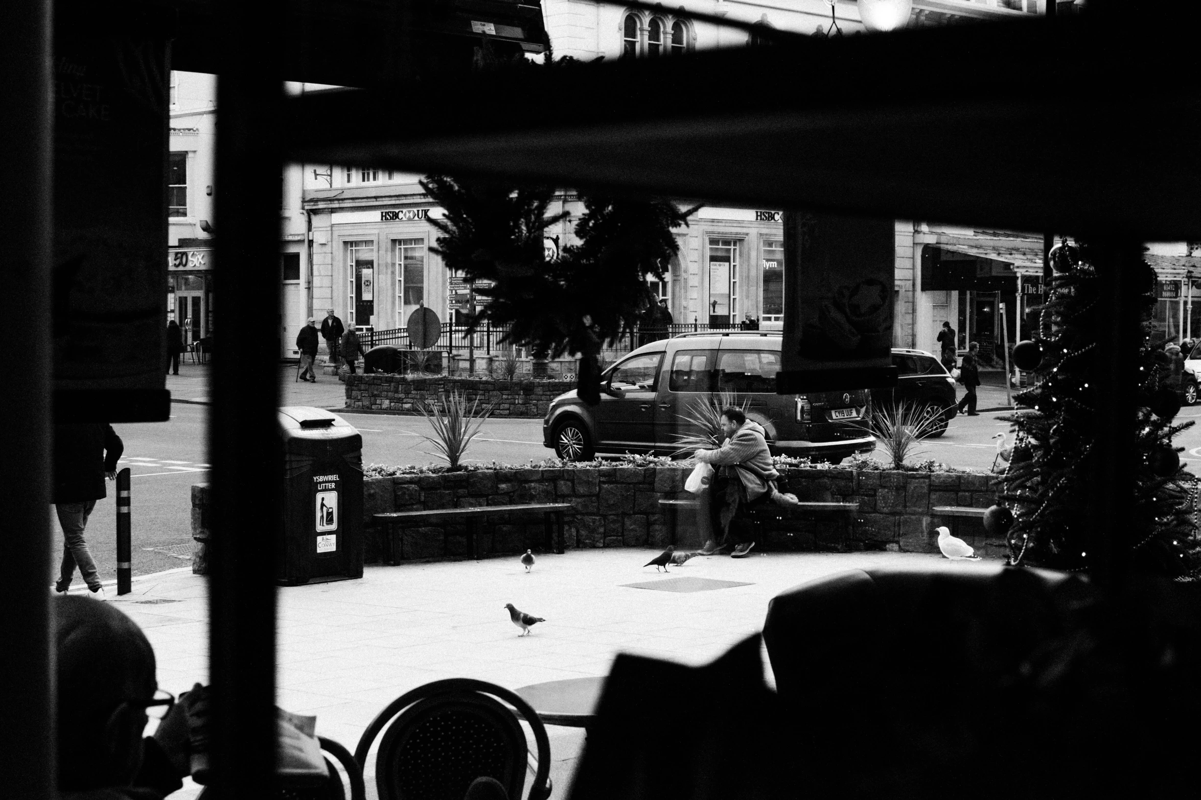 a black and white photo of a person sitting on a bench, a black and white photo, by Tamas Galambos, coffee shop, is looking at a bird, khreschatyk, viewed through the cars window