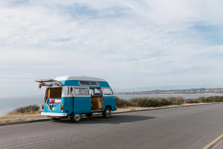 a van that is sitting on the side of a road, by Lee Loughridge, unsplash, bondi beach in the background, clear blue skies, vintage photo, wheres wally