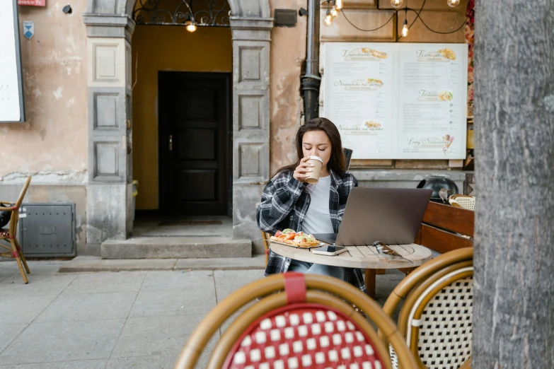 a woman sitting at a table with a laptop, by Julia Pishtar, pexels contest winner, people outside eating meals, drinking coffee at central perk, full body image, ekaterina