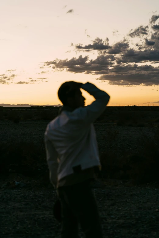 a man that is standing in the dirt, inspired by Russell Drysdale, unsplash, happening, dusk light, side profile shot, half turned around, view from a distance