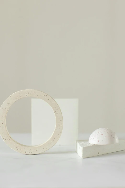 a white object sitting on top of a white table, an abstract sculpture, inspired by Isamu Noguchi, the ring, speckled, centered in a frame, dough sculpture