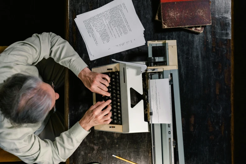 an overhead view of a man typing on a typewriter, a portrait, pexels contest winner, private press, wooden desks with books, on vellum, ignant, thumbnail