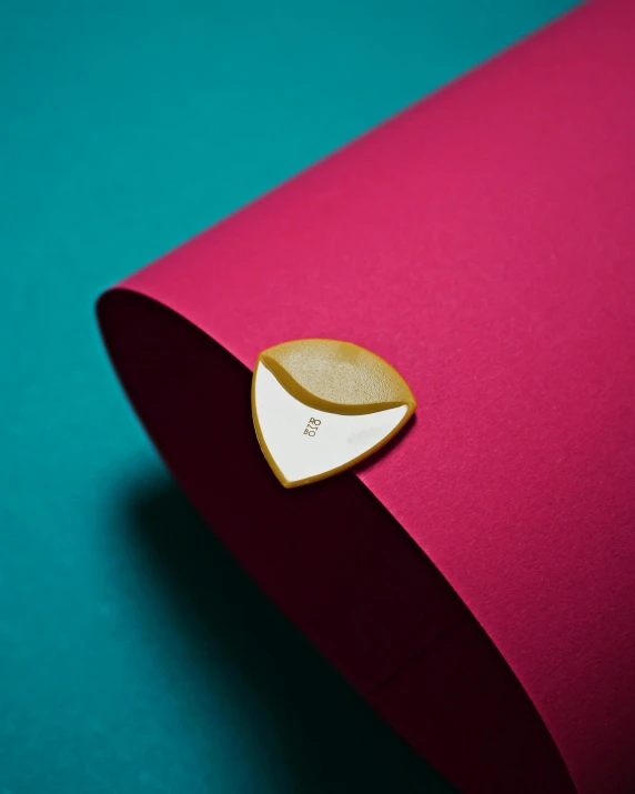 a heart shaped cookie sitting on top of a pink paper, inspired by Lucio Fontana, private press, inlaid with gold, official product photo, badge, lpoty