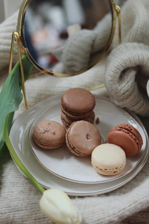 a white plate topped with macarons next to a mirror, a still life, trending on pexels, romanticism, brown colours, made of glazed, stroopwaffel, feature