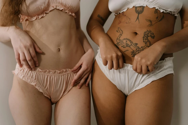 a couple of women standing next to each other, a tattoo, trending on pexels, antipodeans, cute panties, stomach skin, lingeries beauty, pearlescent skin