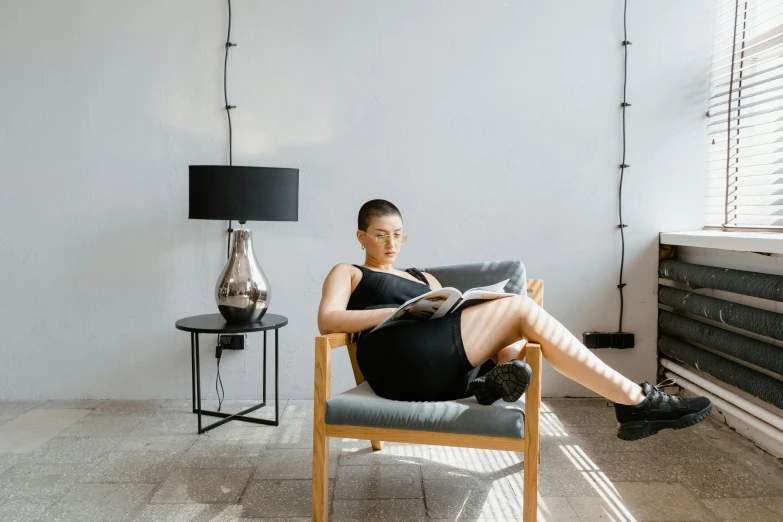 a woman sitting in a chair reading a book, pexels contest winner, wearing black tight clothing, modern gallery furniture, afternoon hangout, lara croft relaxing