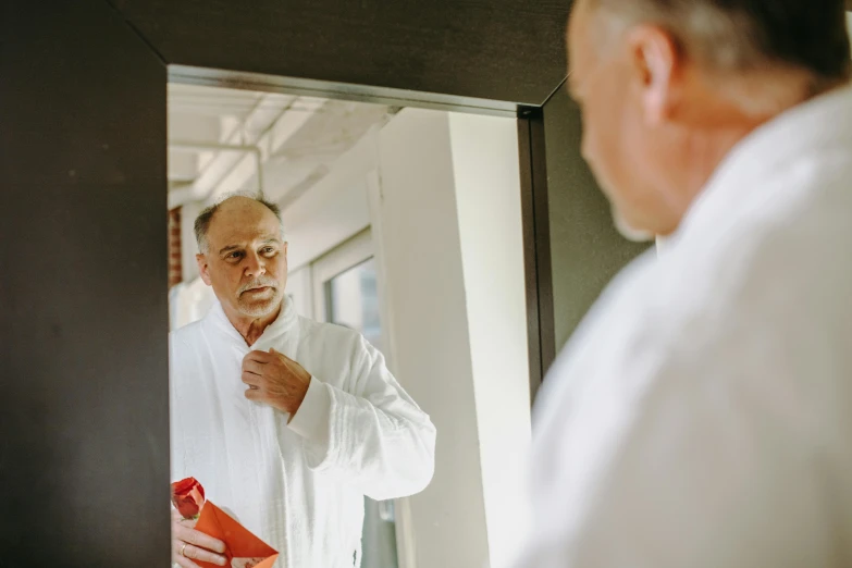 a man adjusting his tie in front of a mirror, pexels contest winner, wearing a white robe, bald man, local conspirologist, about to enter doorframe