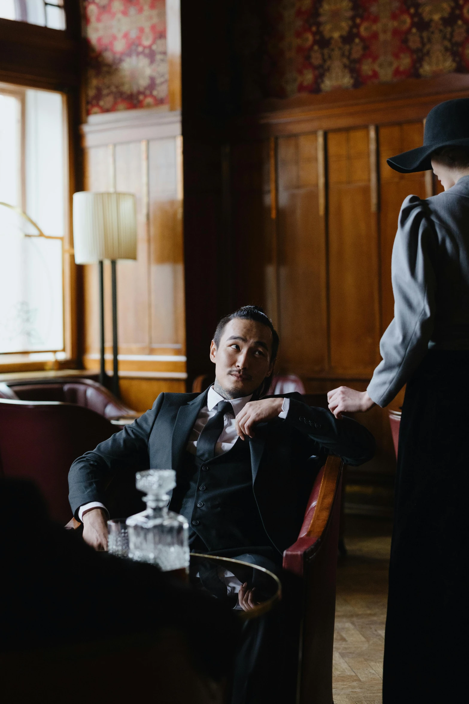 a man sitting in a chair next to a woman, unsplash, art nouveau, joe taslim, a suited man in a hat, indoor scene, slide show