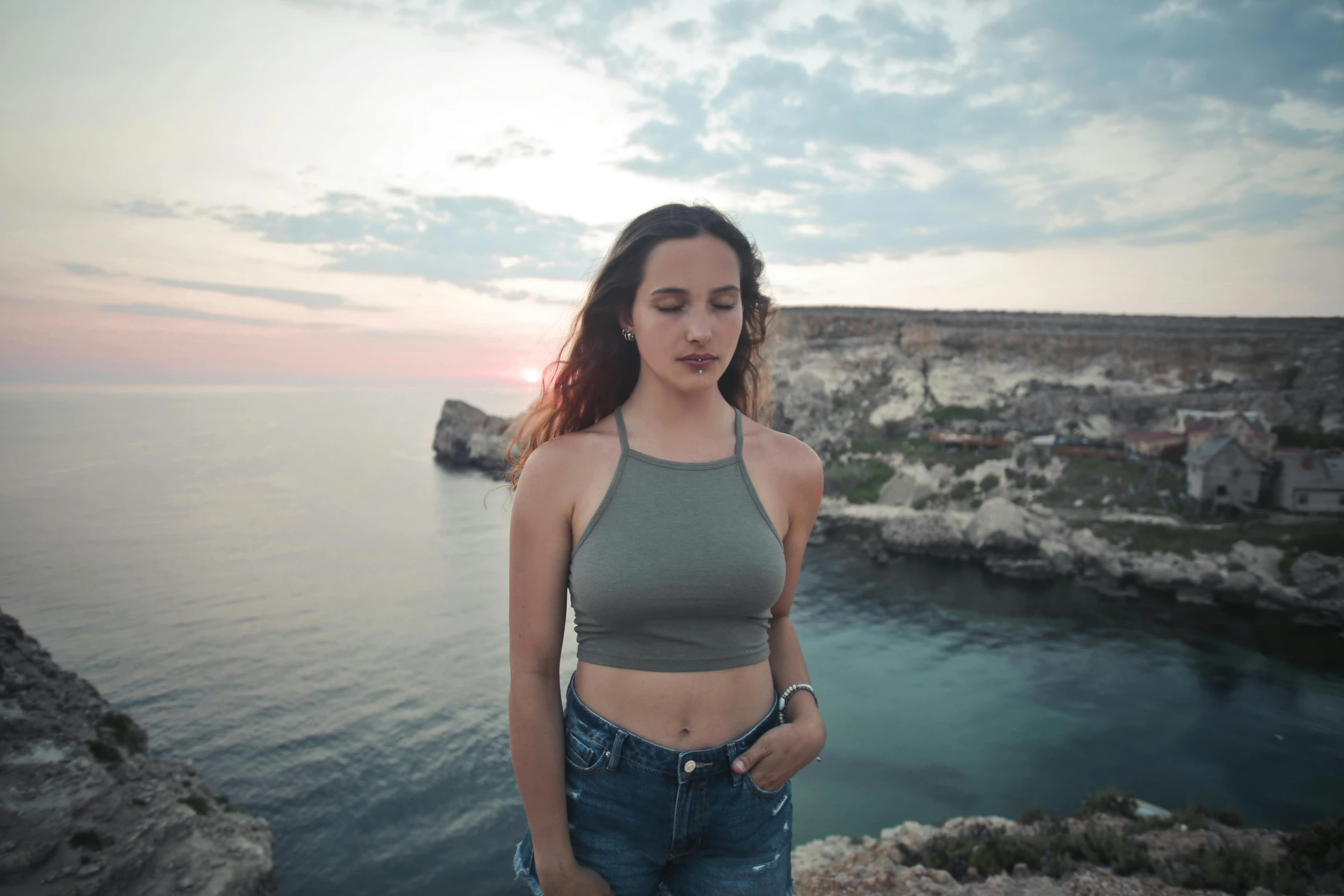 a woman standing on top of a cliff next to the ocean, a picture, inspired by Fede Galizia, pexels contest winner, wearing a cropped tops, portrait of teenage aphrodite, late evening, wearing tank top